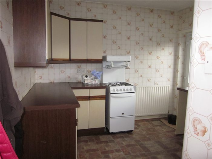 Kitchen before: brown units and patterned wallpaper