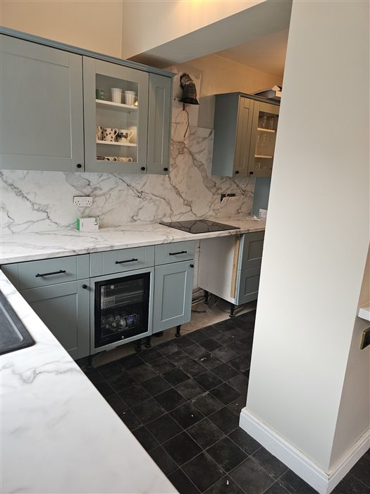 Same kitchen finished: sage shaker units, marble-effect worktop and full-height splashback