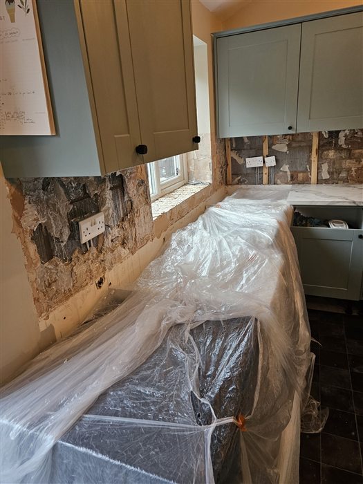 Kitchen during work: new sage units wrapped in plastic while old tiles are stripped back to the brick